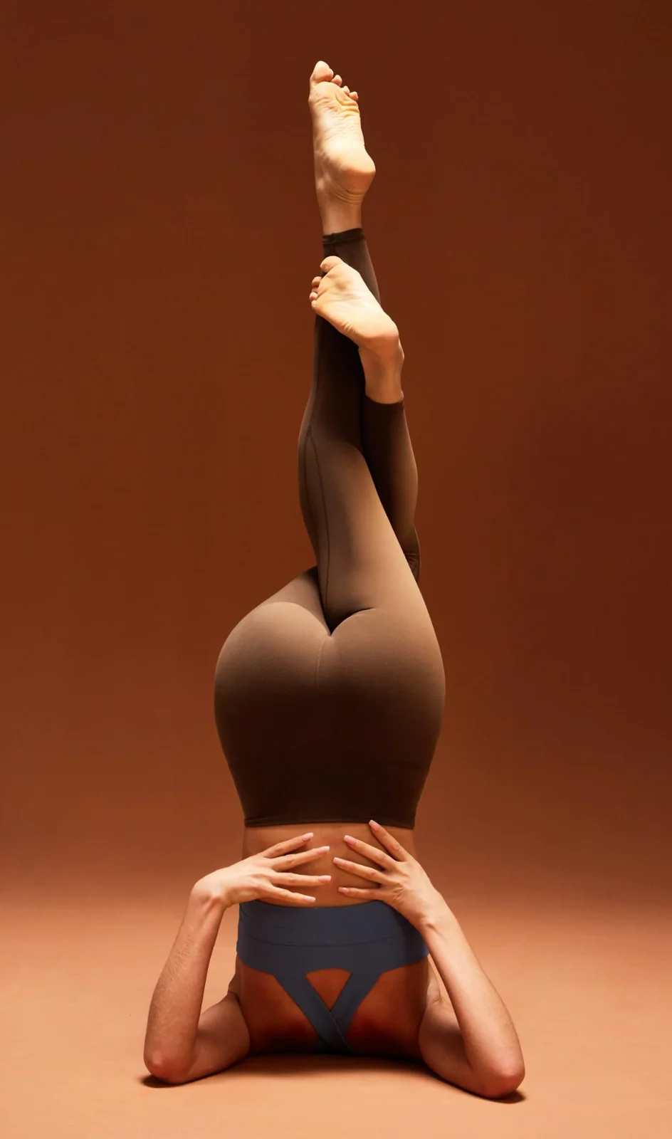 The Ewedoos buttery compression leggings in brown, in a headstand against a terracotta wall